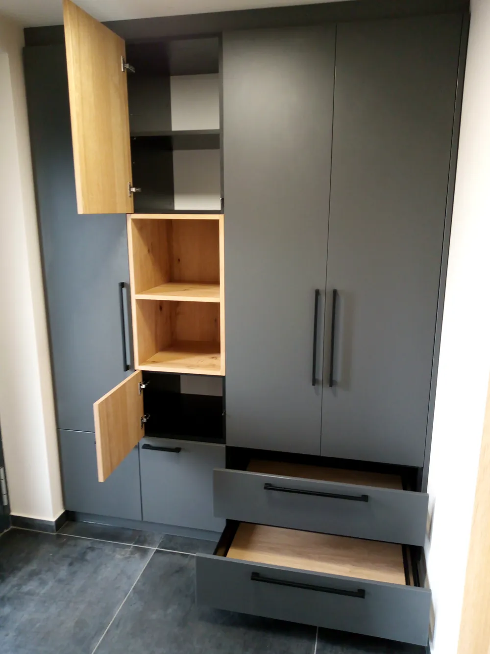 Šatní skříň s dubovými a šedými dvířky a otevřenými zásuvkami
